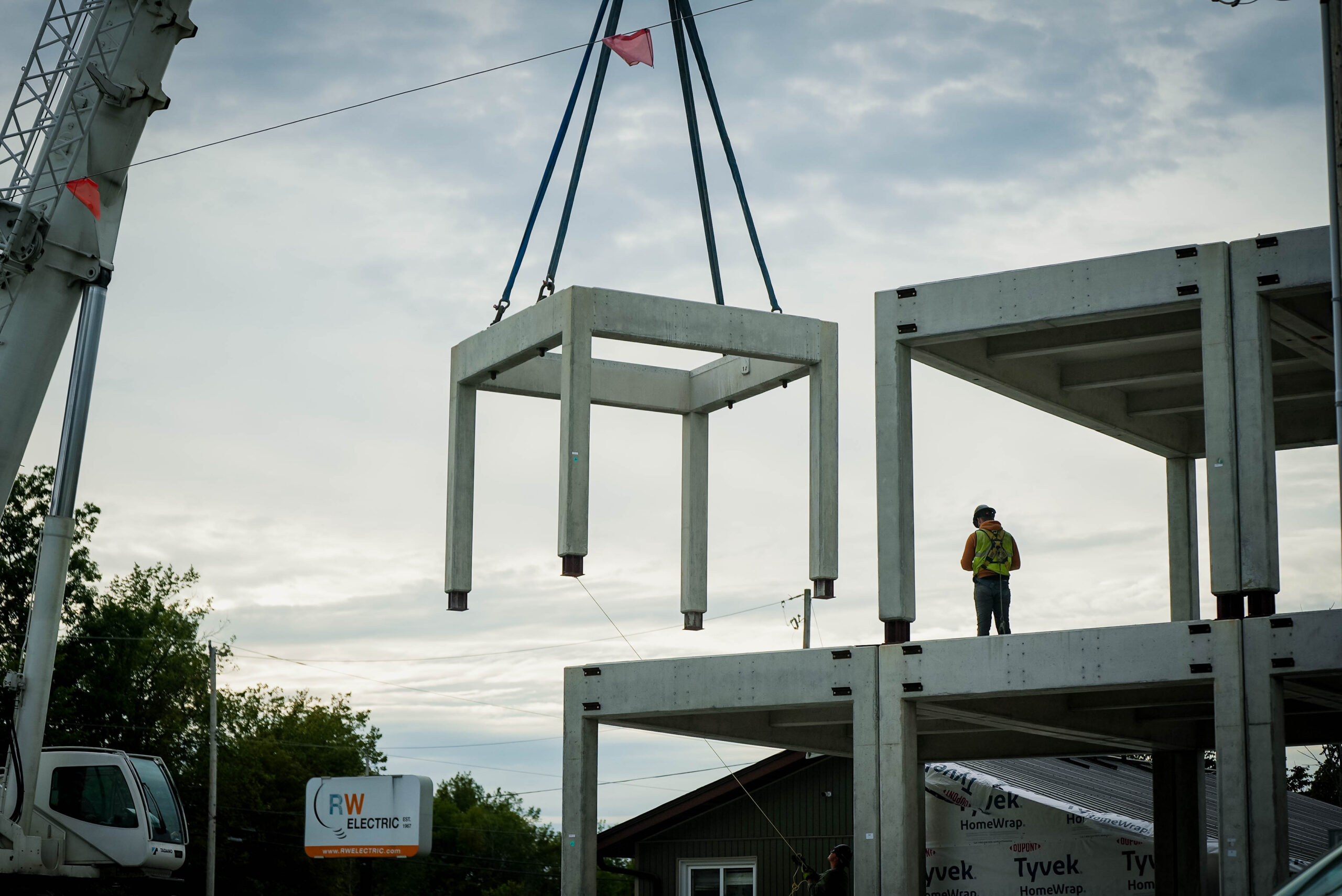 Crane positioning a precast module above an existing structural frame.