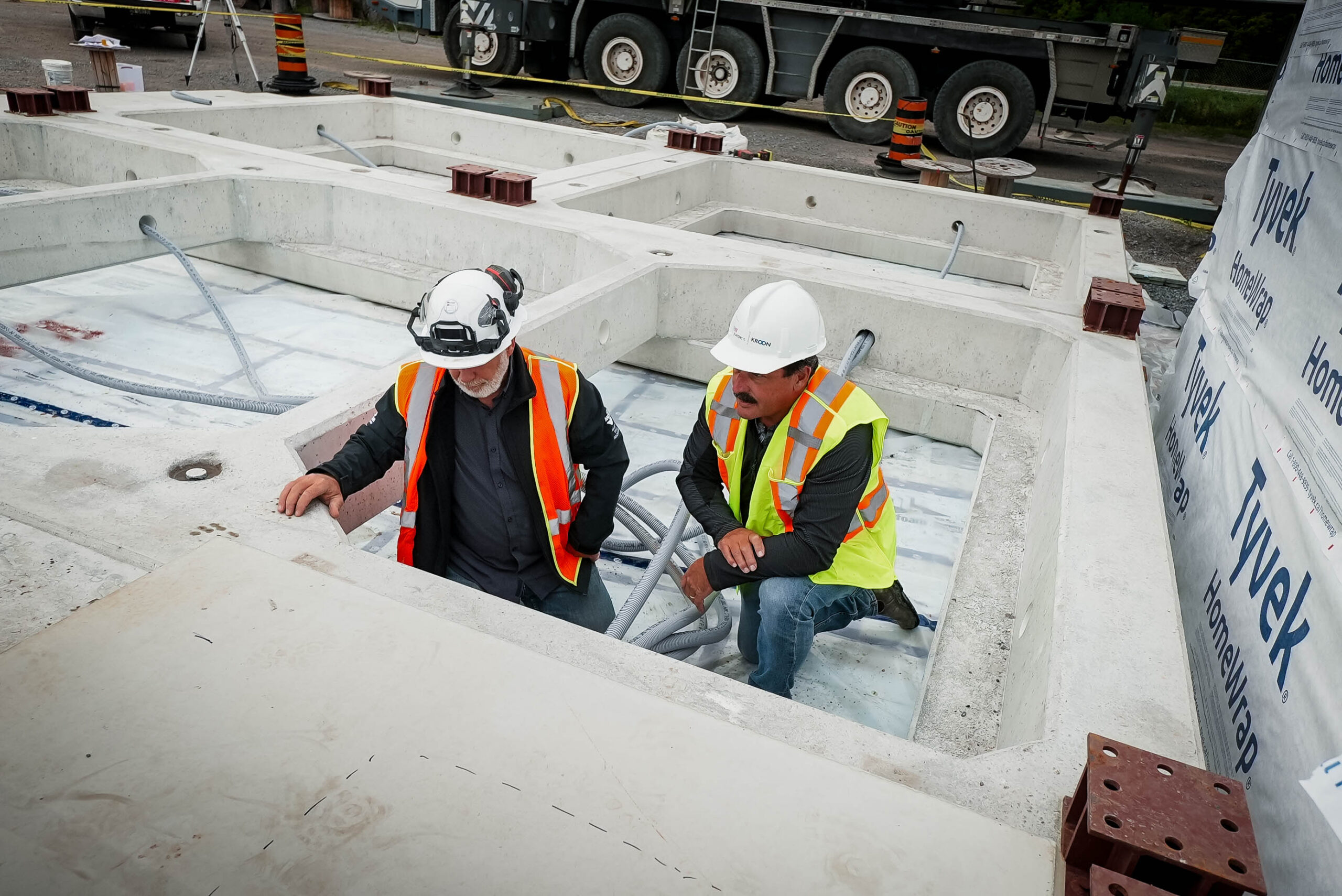 Two workers coordinating installation within prepared precast base elements.